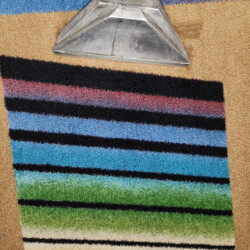 A carpet cleaning tool is shown cleaning a colorful striped carpet, revealing a cleaner section compared to the rest.
