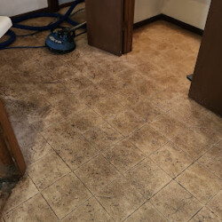 Dirty tiled kitchen floor with visible stains; cleaning equipment and hoses are seen near an open doorway.