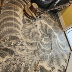 A floor cleaning machine scrubs a tiled floor covered in soapy water in a laundry room.