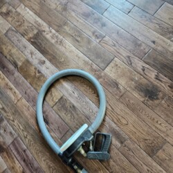 A vacuum hose with a handle attachment lies coiled on a wooden floor.