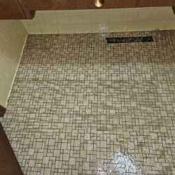 Mosaic tile floor with visible water damage causing warping and discoloration near a wall vent and cabinets.
