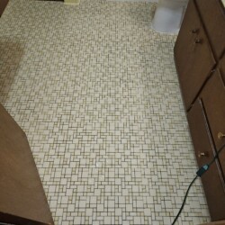 Bathroom with small square and rectangular mosaic tile flooring, wood cabinets, and a white toilet in the background.