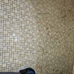A tiled wall half cleaned by a steam cleaner, showing a stark contrast between clean and dirty sections.