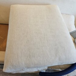 A couch cushion is being cleaned with an upholstery cleaning tool attached to a blue hose.
