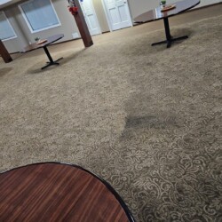A patterned carpeted room with round tables and a noticeable dark stain on the floor near the center.