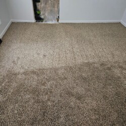 A beige carpeted room with visible vacuum lines and some cleaning equipment visible near the doorway.