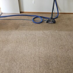 A carpet cleaning machine in use shows a distinct line between cleaned and uncleaned carpet in a room.